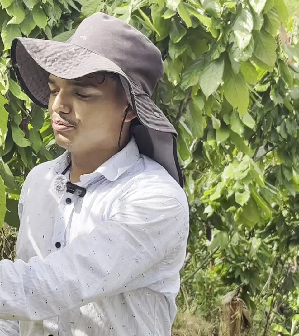 A young grower in a sun hat holding pruning shears among the cacao trees